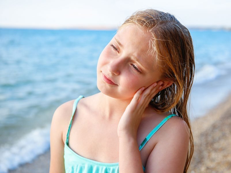 Mädchen am Strand fasst sich ans Ohr