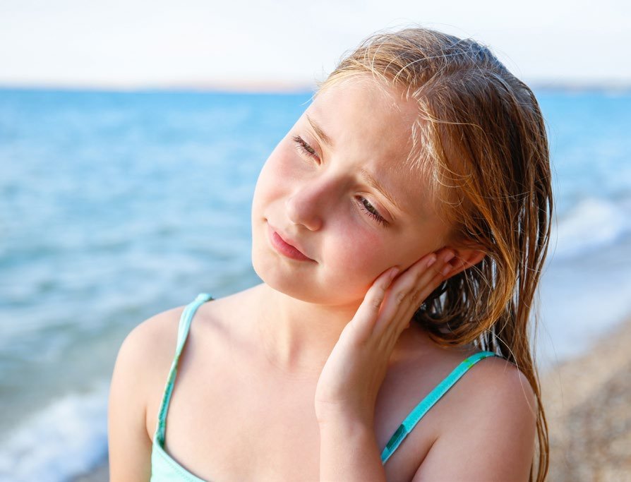 Mädchen am Strand fasst sich ans Ohr