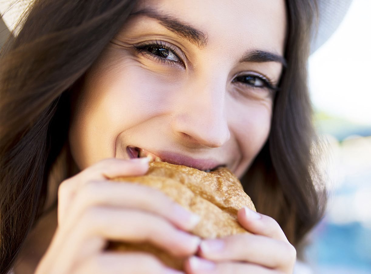 Lachende Frau beißt in ein Brot