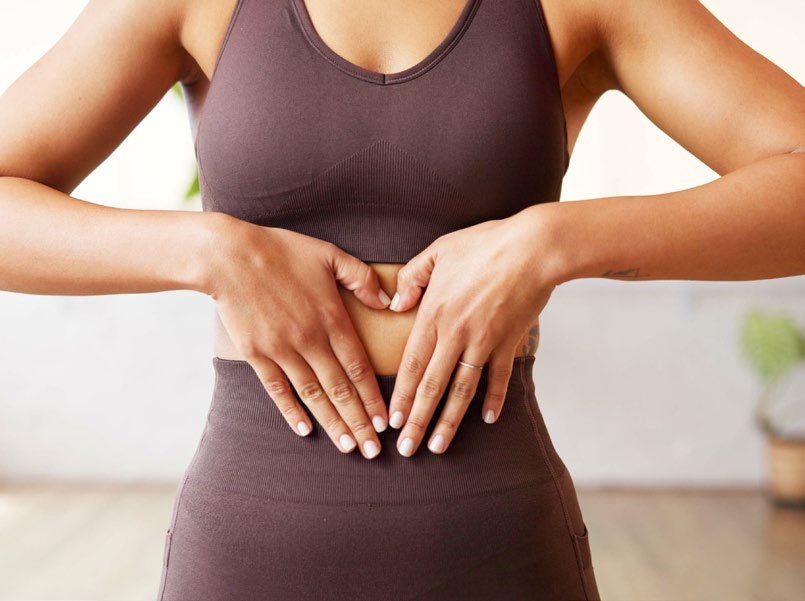 Frau formt mit den Händen ein Herz auf dem Bauch