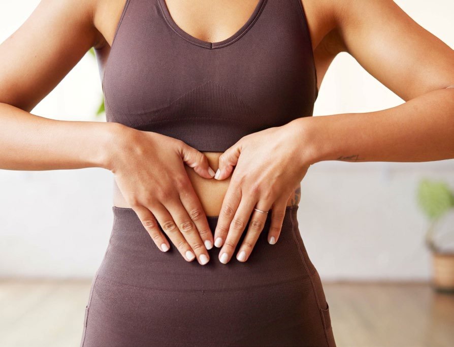 Frau formt mit den Händen ein Herz auf dem Bauch